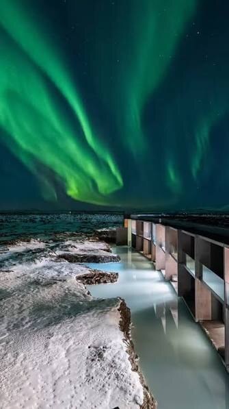 Northern lights over a steaming lagoon in the snow