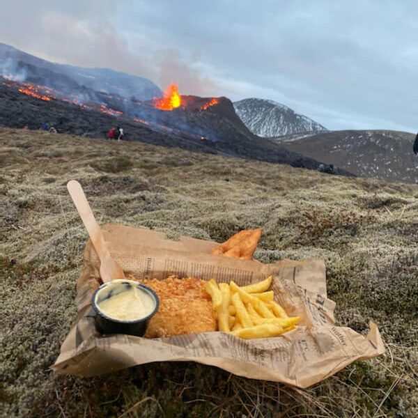A box of Issi fish and chips on the moss in front of an erupting volcano