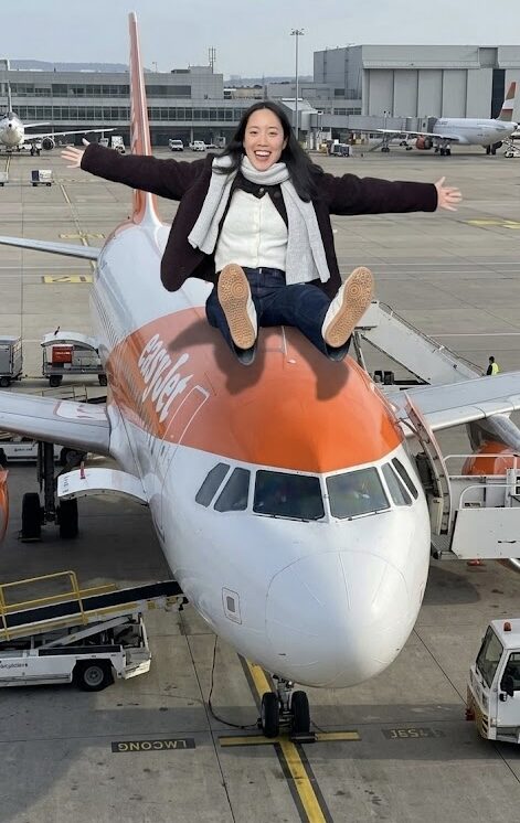 Megan sitting on top of an easyJet plane, arms wide