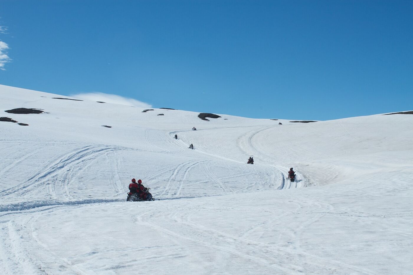 Snowmobiles crossing a white glacier under a blue sky